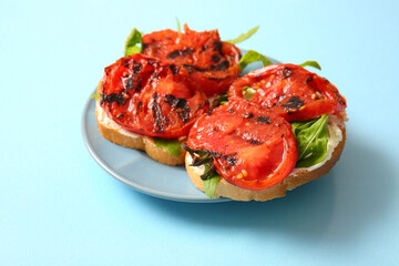 Plate of sandwiches with tasty grilled tomatoes and arugula on blue background