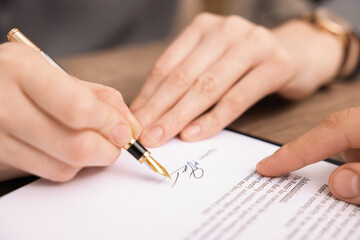 Man pointing at document and woman putting signature at table, closeup