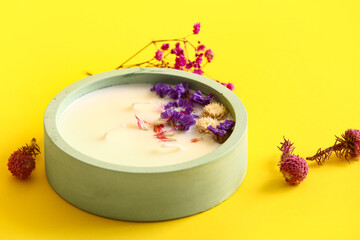 Holder with candle and flowers on yellow background