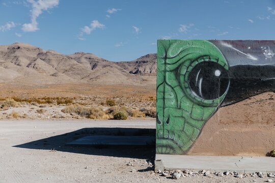 Alien graffiti art on a building in the Nevada desert. The mural depicts a green alien head and stars, adding an otherworldly element to the arid landscape.  Hiko, Nevada, USA. 0 October 2024