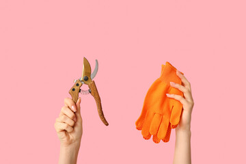 Female hands with secateurs and gloves on pink background, closeup