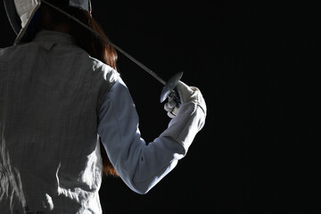 Fencer with epee on black background, back view. Space for text