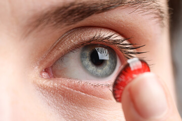 Woman putting in red color contact lens, closeup