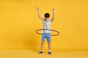 Boy exercising with hula hoop on yellow background