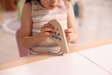 Motor skills development. Little girl playing with wooden lacing toy indoors, closeup