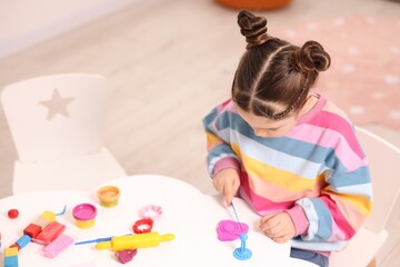 Motor skills development. Little girl playing with colorful dough at table indoors