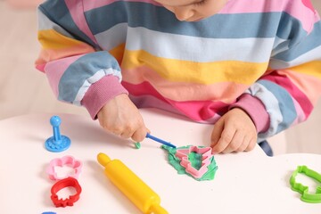 Motor skills development. Little girl playing with colorful dough at table indoors, closeup