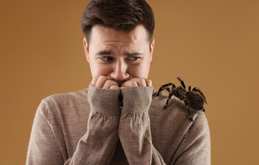 Scared man with spider on his shoulder against pale brown background. Arachnophobia concept