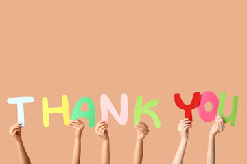 Female hands holding text THANK YOU made of paper on brown background
