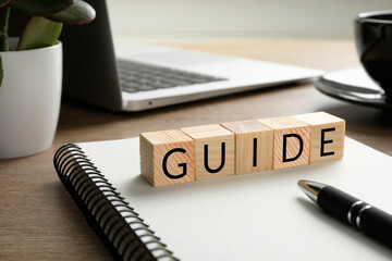 Word Guide made of cubes, notebook and pen on wooden table