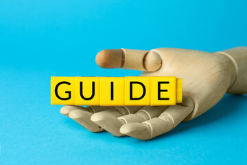 Mannequin hand holding cubes with word Guide on light blue background