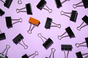Difference, uniqueness, individuality. Orange binder clip among black ones on violet background,...
