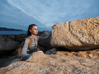 Young woman hiking on rocky coastline during sunset, wearing casual outdoor clothing, reflecting peaceful emotions in natural setting