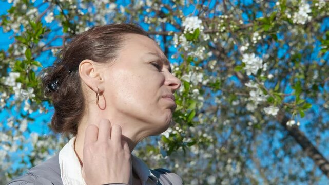 Scratching neck during allergy. A view of stressed female scratching her skin because of pollen allergy during spring promenade in the park.