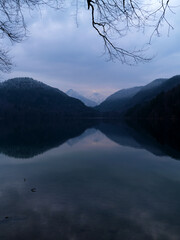 Tranquil lake surrounded by mountains during twilight hours near a serene forest setting