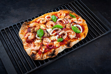 Traditional Italian pinsa bread prosciutto e salsa di pomodoro with seafood, buffalo mozzarella and tomato sauce served as close-up on a rustic cast iron grillage