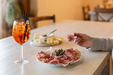 A cozy aperitivo moment featuring a refreshing Aperol Spritz, a plate of assorted cured meats with pickles, and a platter of fine cheeses. Warm atmosphere and rustic table setting