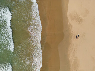 Drone view of a couple walking on the sandy beach.