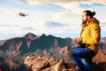 Naklejka premium Modern traveler creating content and filming the valley with his drone, climbing on top of a high altitude mountain range. Hiker enjoying the landscape scenery, remote control.