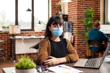 Caucasian female analyst sitting with her arms crossed at office desk and looking at camera....
