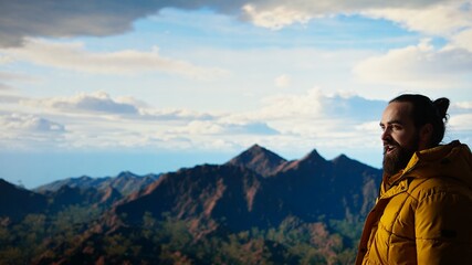 Naklejka premium Thrilled traveler raises his arms in triumph after climbing the mountain top, enjoying the panoramic beauty of the nature. Feeling proud and admiring the vast sky and endless landscape. Camera A.