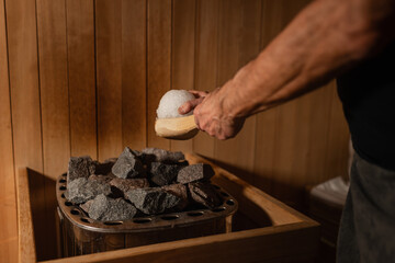 A person places an ice ball on hot sauna stones, creating a burst of steam. This contrast between...