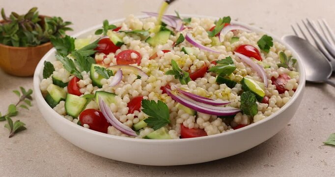Pearl couscous salad with red onion, herbs and tomatoes, drizzling with olive oil