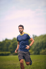 Fototapeta premium Morning, exercise and man on grass for running challenge, wellness and healthy outdoor fitness. Training, cardio and runner in park in nature with commitment, progress and athlete in workout.