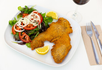 Breaded pork with fresh salad with onions and tomatoes. Serving Spanish pork with vegetables on a...