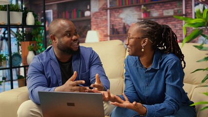 African american young freelancers on couch sharing a business idea, using modern technology and...