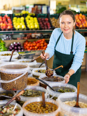 in vegetable department, friendly woman - owner of store puts large olives into container for buyer
