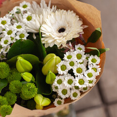 Wrapped bouquet of green and white flowers, .Spring bouquet close-up in craft paper. Floral wallpaper.