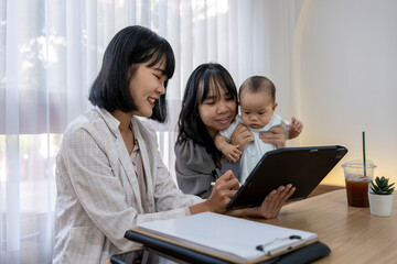 A woman is holding a baby while looking at a tablet