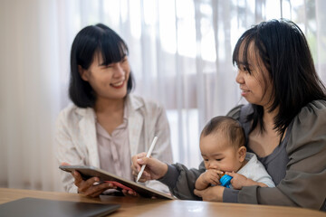 A woman is holding a baby and writing on a tablet