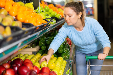 experienced hostess came to supermarket of vegetables and fruits. She chooses juicy apples in window