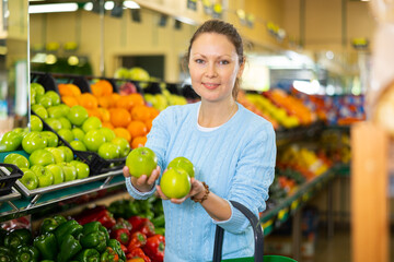 experienced hostess came to supermarket of vegetables and fruits. She chooses juicy apples in window