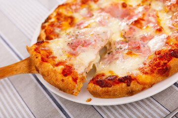 Cooked delicious pizza with stretchy cheese and prosciutto. Appetizing slice of Italian pizza on a plate close-up