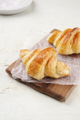 Freshly baked croissants placed on a wooden board with parchment paper, showcasing their golden, flaky layers.