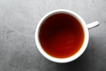 Refreshing black tea in cup on grey textured table, top view. Space for text