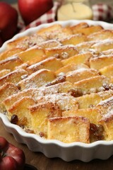 Delicious bread pudding with raisins, powdered sugar and apples on wooden table, closeup