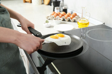 Woman taking fried eggs from frying pan in kitchen, closeup