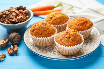 Tasty carrot muffins and walnuts on light blue wooden table, closeup