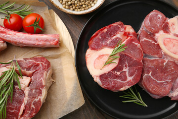 Pieces of raw beef, rosemary and tomatoes on wooden table, flat lay