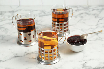 Glasses of tea in metal holders served on white marble table, closeup