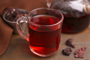 Fototapeta premium Delicious hibiscus tea in glass cup, teapot and dry roselle sepals on wooden table, closeup
