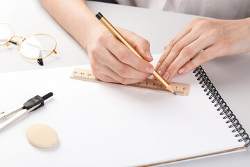 Woman drawing sketch with ruler and pencil on notebook at white table, closeup