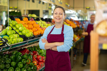 in supermarket of farm products, friendly woman seller of vegetable department is waiting for buyers