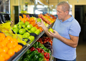 Concentrated mature male buyer pensioner choosing organic granny smith green apples in hypermarket