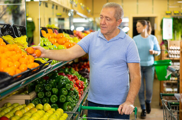Elderly male pensioner in casual wear choosing local tangerines fruits in grocery store