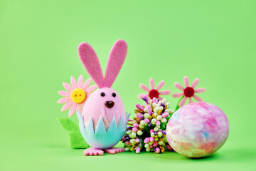 cute toy pink bunny celebrating Easter with a big colorful egg and flowers on a green background